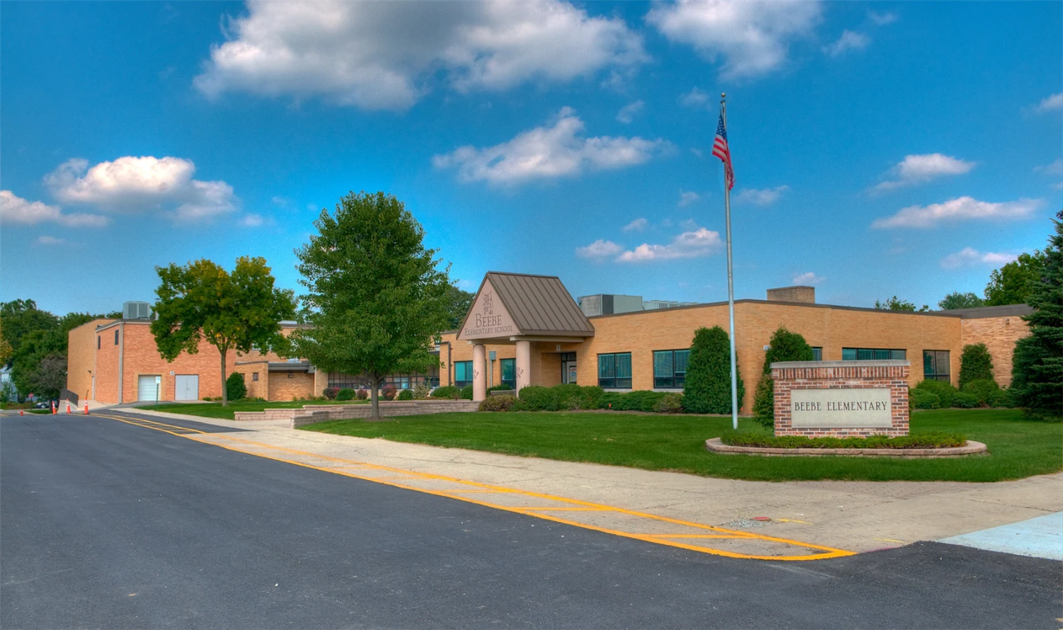 Exterior of Beebe Elementary School in Naperville, Illinois with school sign, American flag, and landscaped grounds