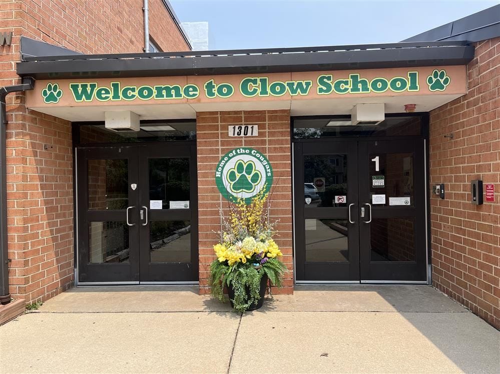 Exterior entrance of Clow Elementary School in Naperville featuring the Welcome to Clow School sign and Cougars mascot logo.