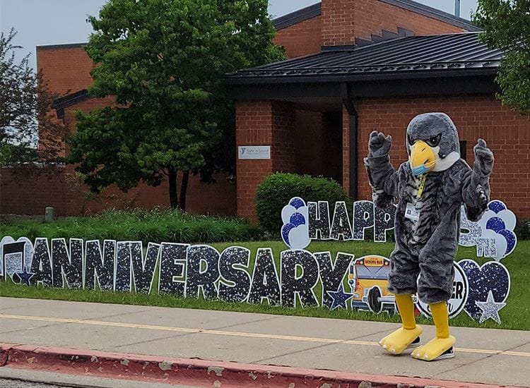 Graham Elementary School mascot Falcon standing next to a Happy Anniversary sign outside the school building in Naperville.