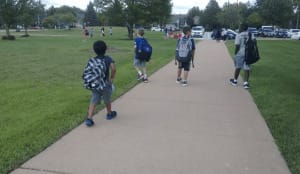 Students with backpacks walking on a paved path toward Kendall Elementary School in Naperville.