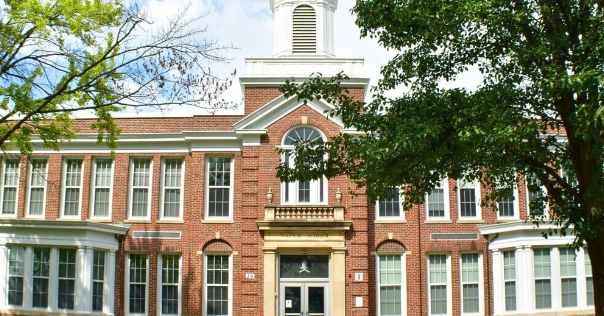 Historic red brick exterior of Naper Elementary School in downtown Naperville featuring a white cupola and stone entrance.