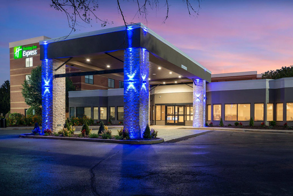 Places to Stay 16 Holiday Inn Express hotel exterior in Naperville, Illinois with illuminated covered entrance at sunset.