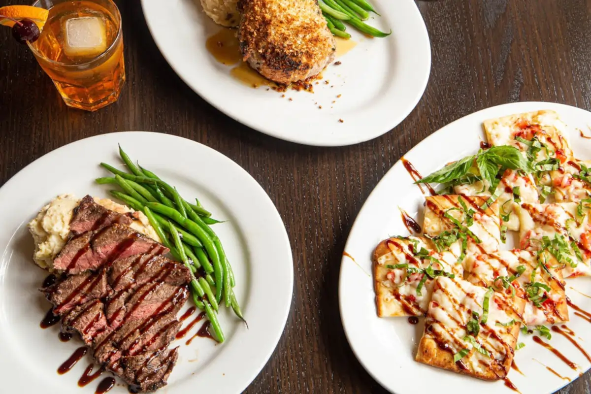 Plated dishes at Ivy Restaurant in Wheaton, Illinois, featuring steak, seafood flatbread, vegetables, and cocktails in an upscale local dining setting
