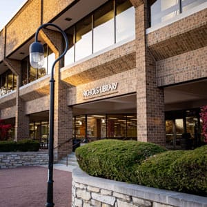 Nichols Library exterior in Downtown Naperville with brick building, entrance sign, landscaping, and walkway for Naperville Public Library visitors.