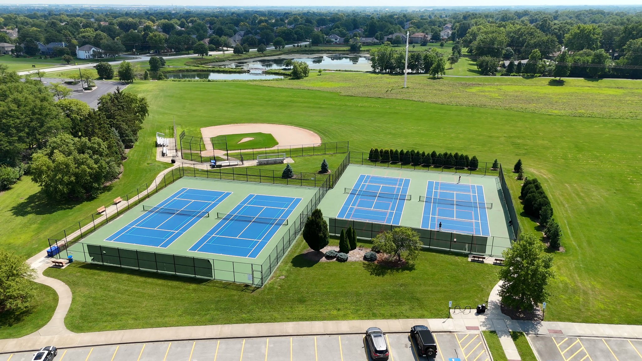 Aerial view of the Ashbury Park tennis courts lined for pickleball, a baseball diamond and ponds in Naperville