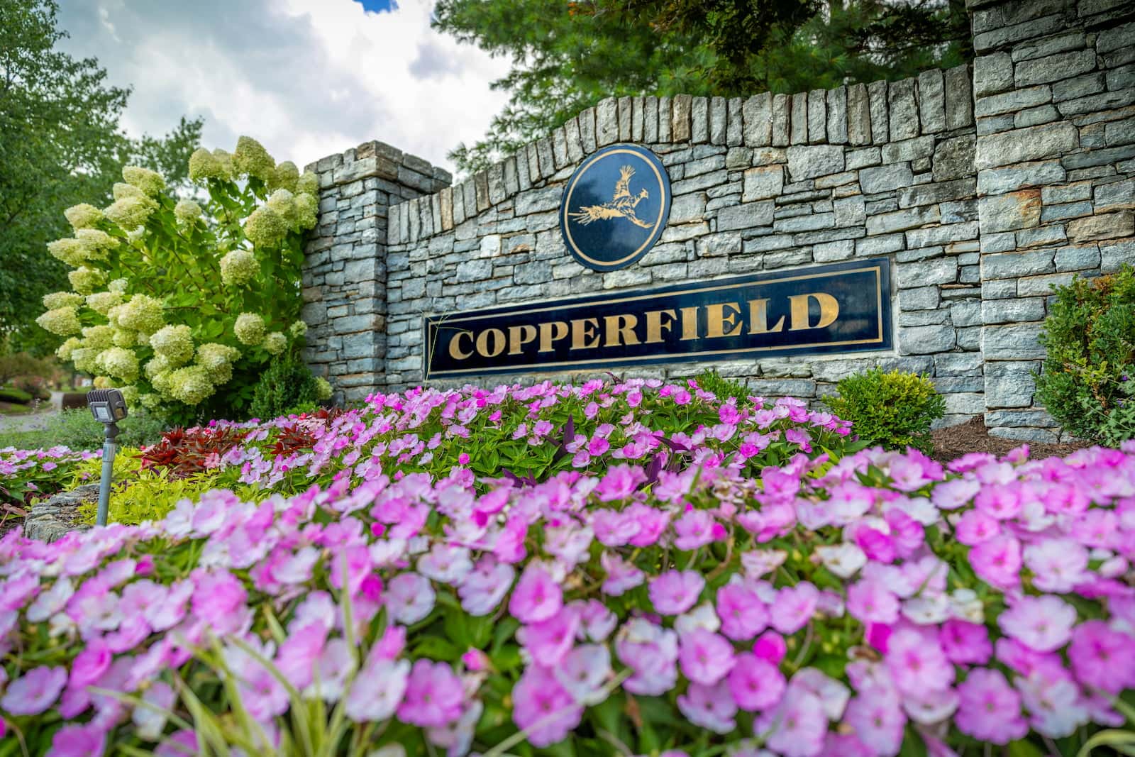 Neighborhoods 4 Copperfield entrance sign on a stone wall with pink flowers in the foreground in Naperville Illinois