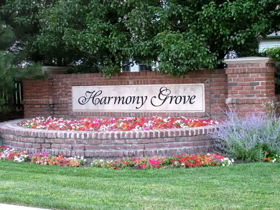 Harmony Grove subdivision entrance sign in Naperville with brick monument, flowers, lawn, and mature trees.