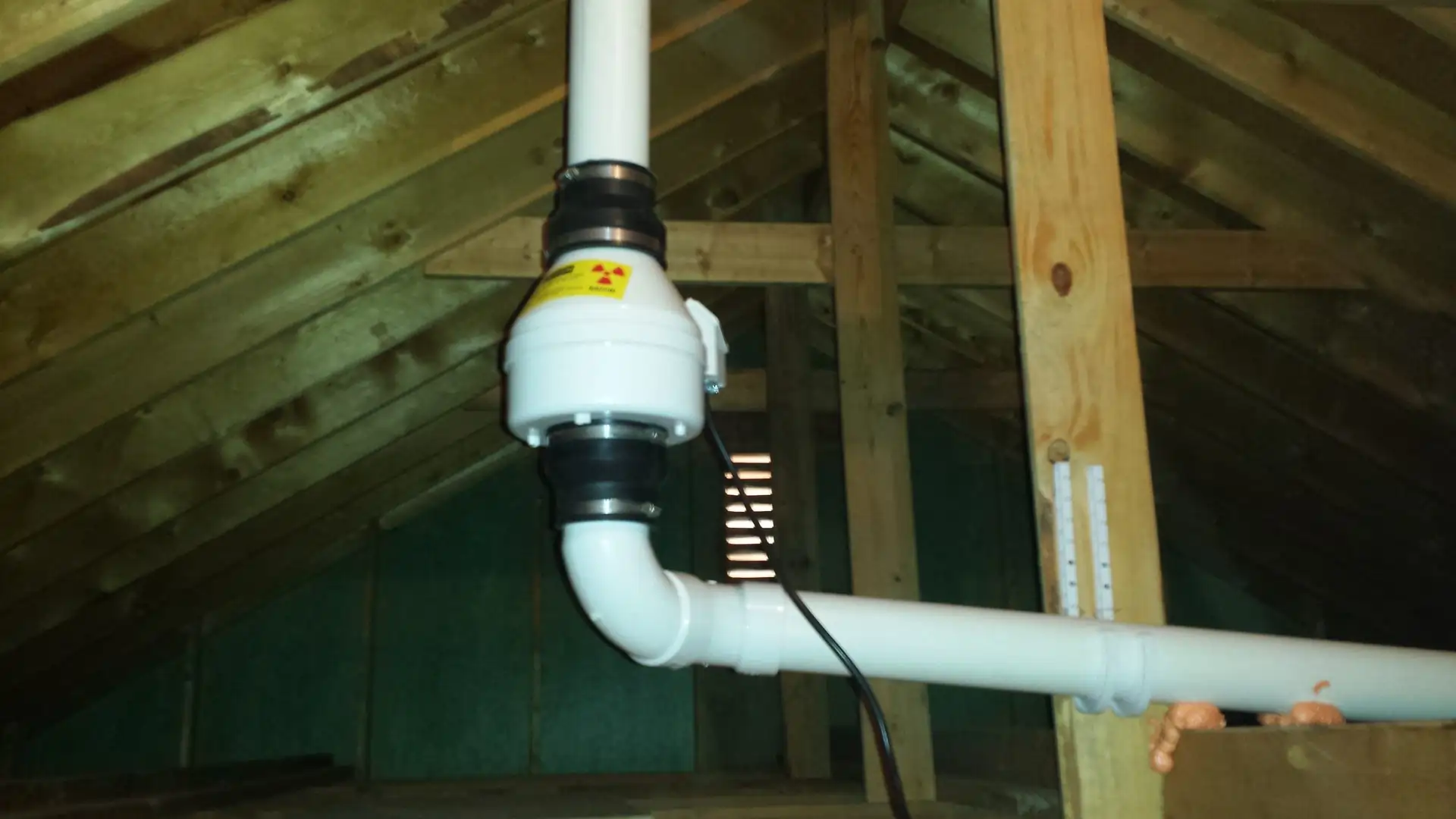 Attic radon mitigation fan and PVC vent piping installed by Heritage Radon Mitigation Services.