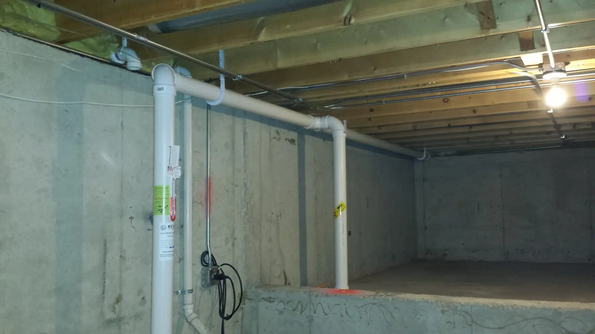 Basement radon mitigation system with PVC vent piping installed by Heritage Radon Mitigation Services.
