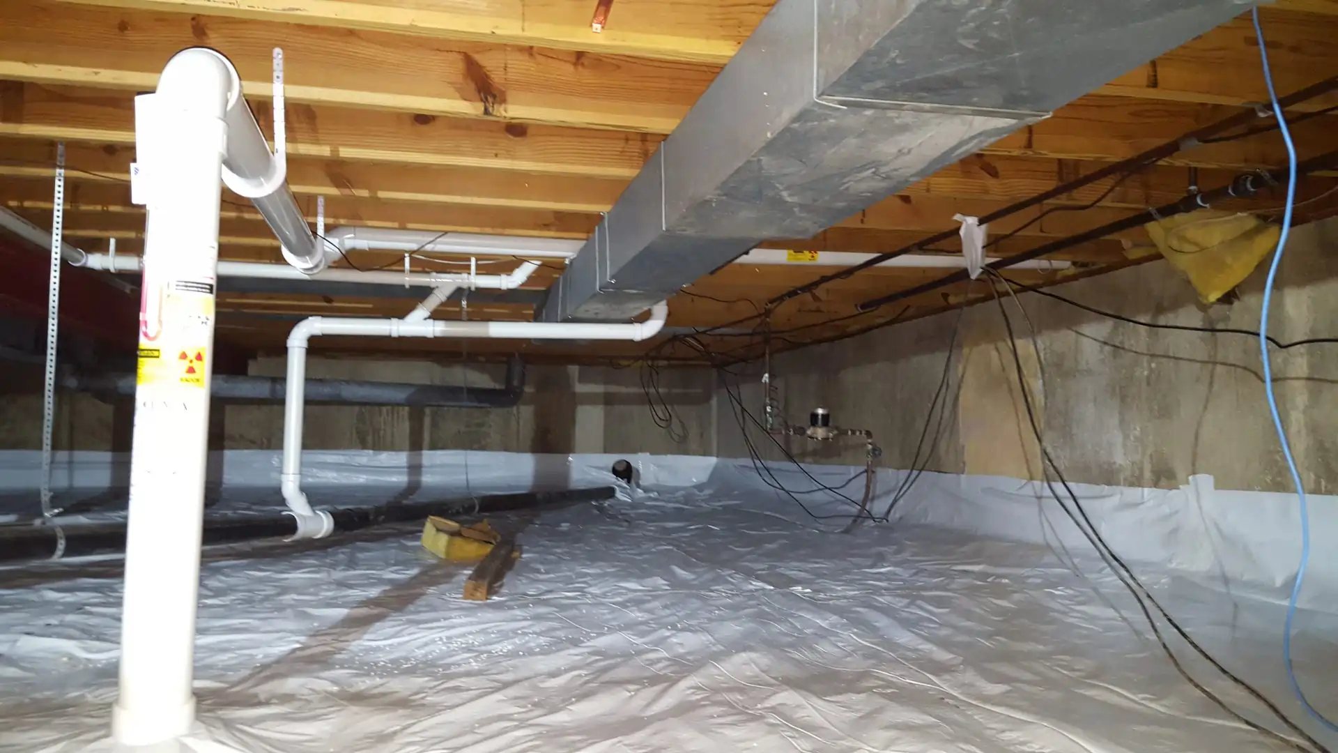 Crawl space radon mitigation system with vapor barrier and PVC vent piping by Heritage Radon Mitigation Services.