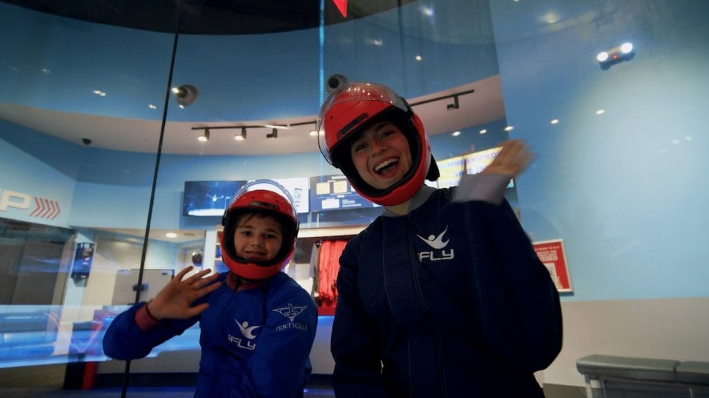 Child and adult wearing red helmets and blue iFLY flight suits ready for first indoor skydiving experience at Naperville location 2026