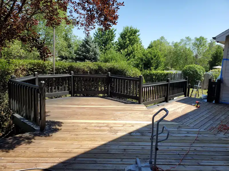 Deck renovation project by JG Home Improvement Corporation showing wood decking, dark railings, and backyard landscaping.