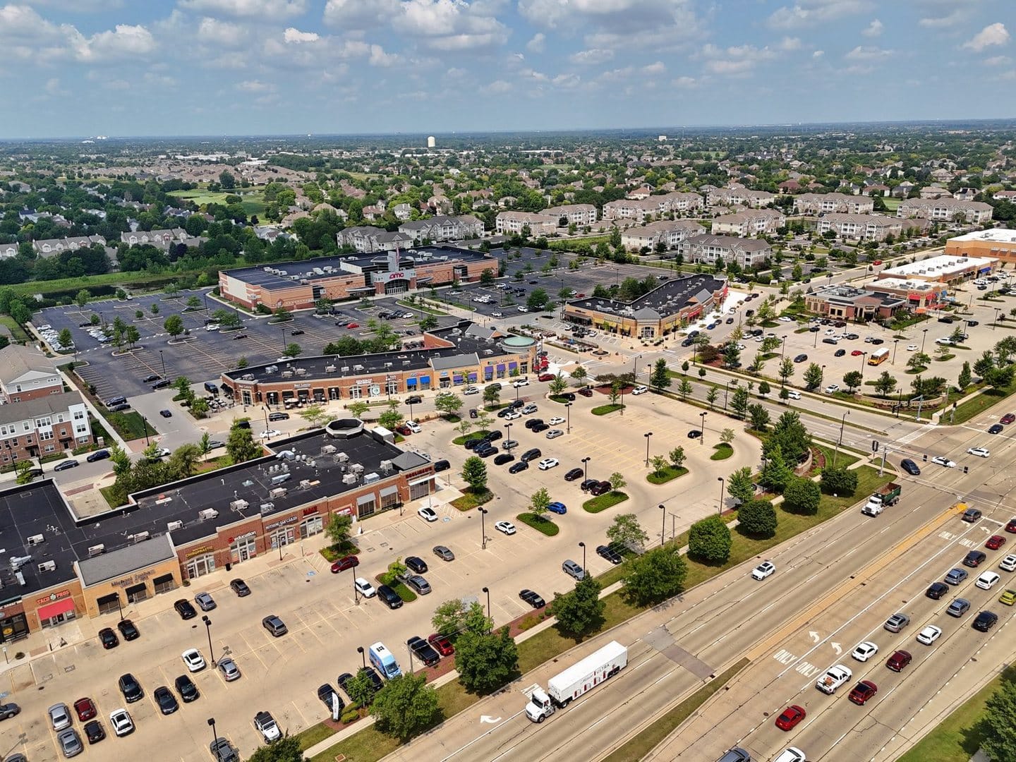Aerial view of Naperville Crossings shopping center, with three-story apartment-style buildings beyond its parking lots