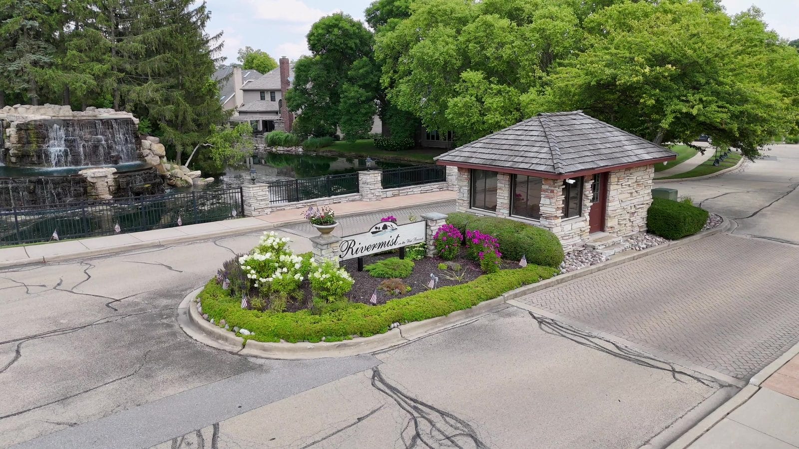 Rivermist entrance with a stone gatehouse, flower beds, waterfall and pond in Naperville