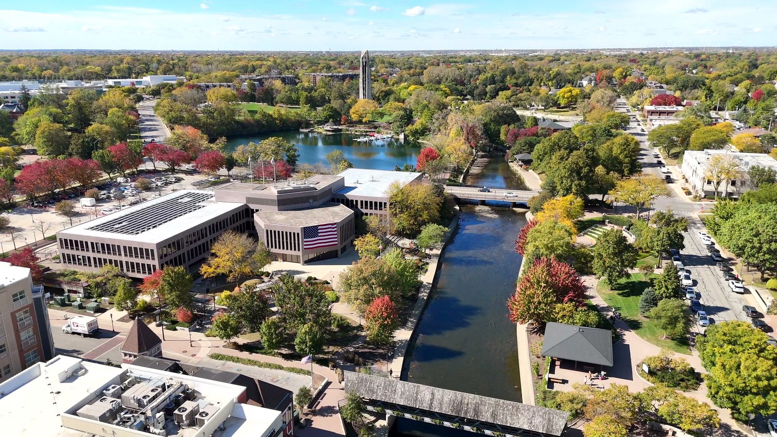 Naperville Halloween and Fall Events 2026: Things to Do Oct 10 to Nov 5 5 Naperville Municipal Center with a large flag beside the Riverwalk and DuPage River in fall