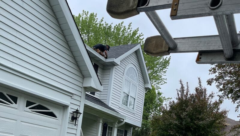 Window cleaning technician working on the upper exterior of a residential home for New Vista Window Cleaning services in the Naperville area.