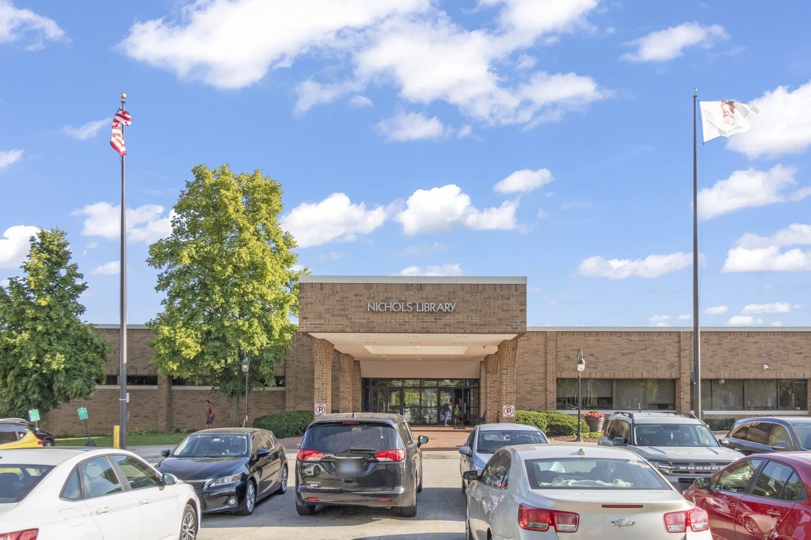 Nichols Library entrance in downtown Naperville with flags and parked cars