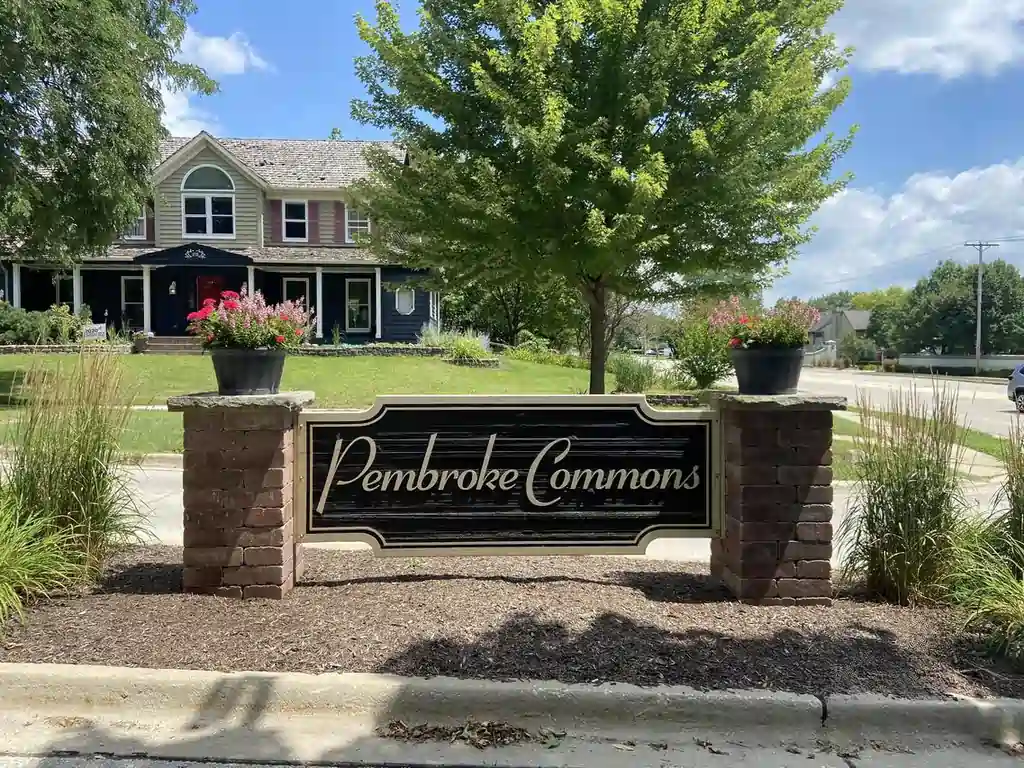 Pembroke Commons subdivision entrance sign in Naperville with brick pillars, planters, landscaping, and nearby homes.