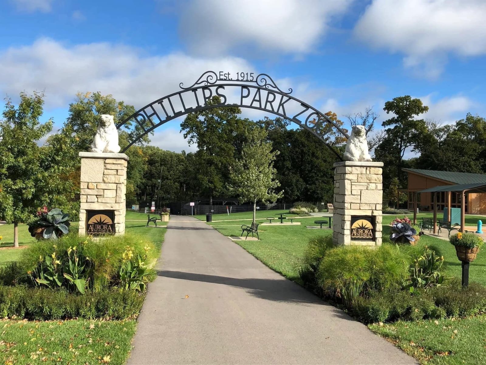 Entrance arch at Phillips Park Dog Park in Aurora, Illinois with landscaped grounds, walkway, and park benches.