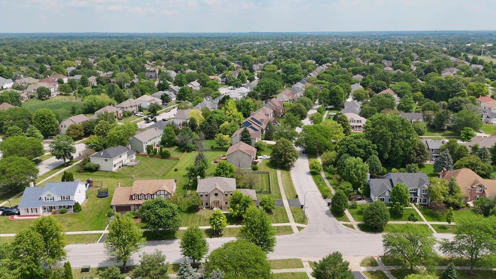 Radon in Naperville homes: high summer aerial of rooftops, tree canopy and curving streets