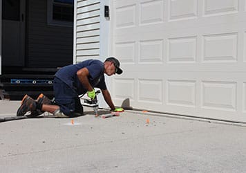Concrete lifting technician working on a residential driveway slab near a garage for concrete repair services in the Naperville area.