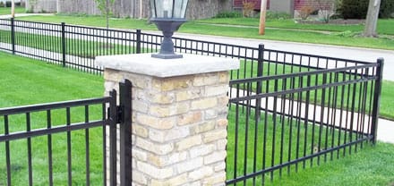 Black metal fence with brick pillar around a residential yard for fence installation and repair services in the Naperville area.