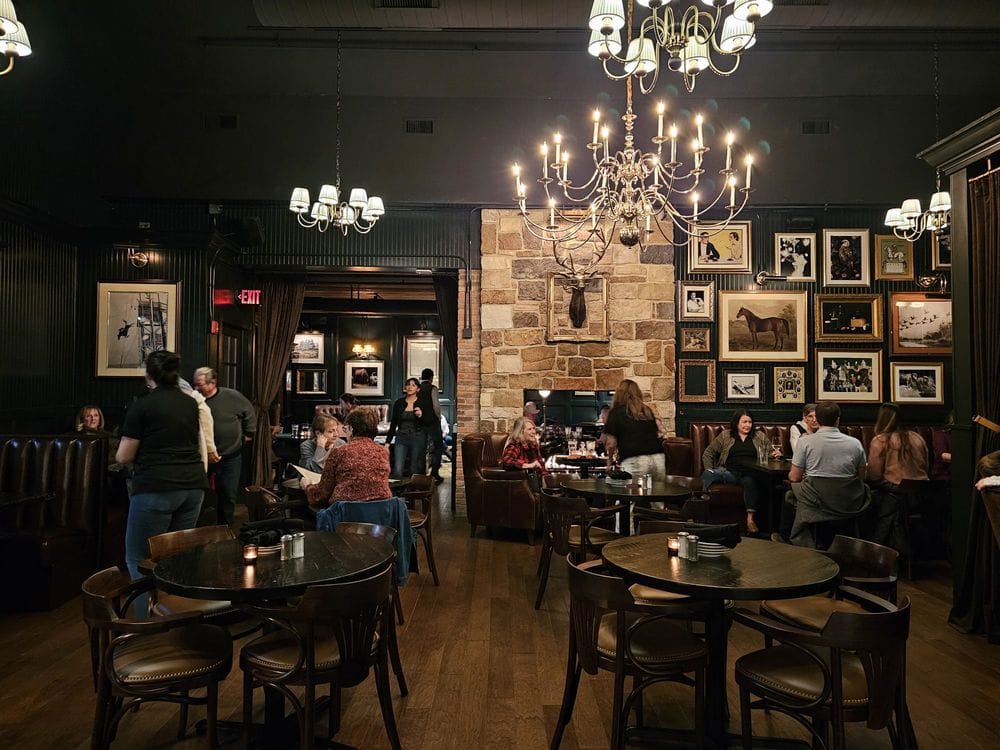 Dining room interior at The George in Naperville, Illinois, featuring chandeliers, stone fireplace, and guests enjoying a local restaurant and downtown Naperville dining atmosphere