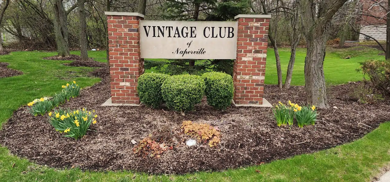 Neighborhoods 3 Vintage Club of Naperville entrance sign with brick pillars and spring flowers in Naperville Illinois