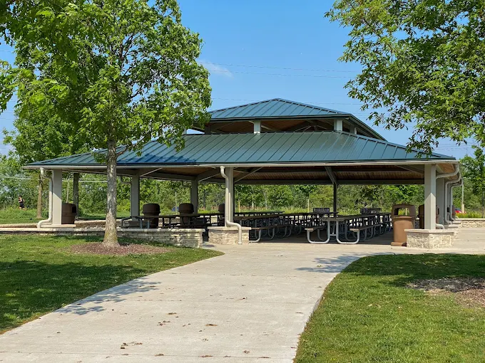 Picnic shelter at Whalon Lake in Naperville, Illinois with tables, paved walkway, trees, and open park space.