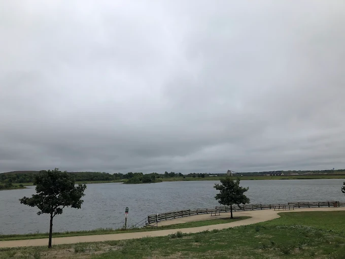 Waterfront trail at Whalon Lake in Naperville, Illinois with lake views, trees, and cloudy sky.