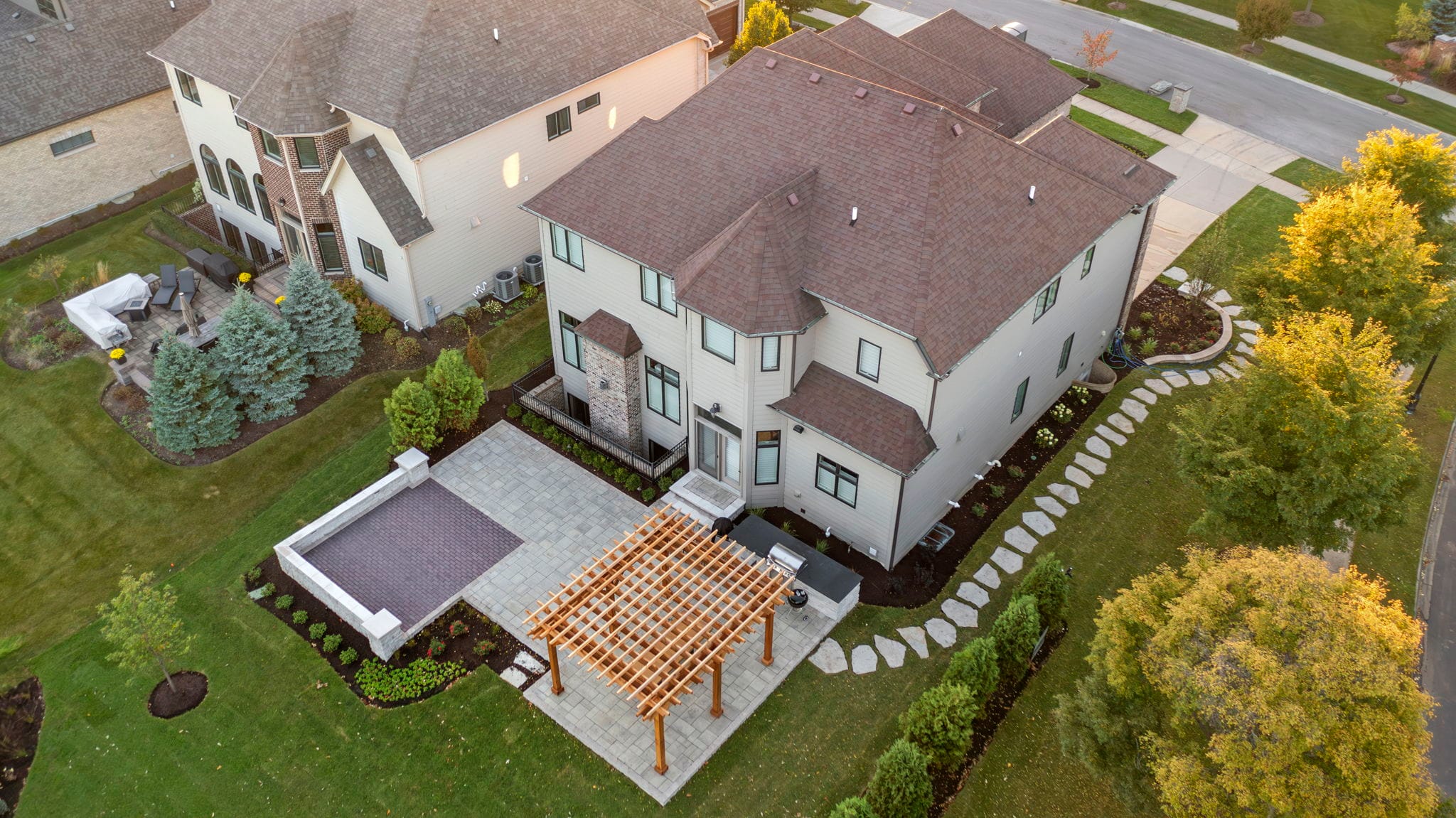 Aerial view of a backyard paver patio with a cedar pergola, seating wall, and stepping-stone path in autumn