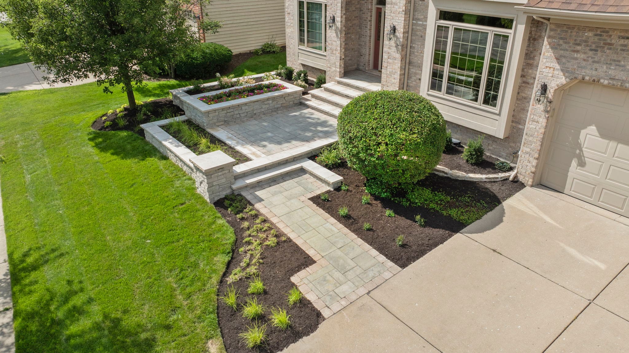 Aerial view of a brick home's front entrance with a raised paver stoop, block planter walls, and a paver walkway