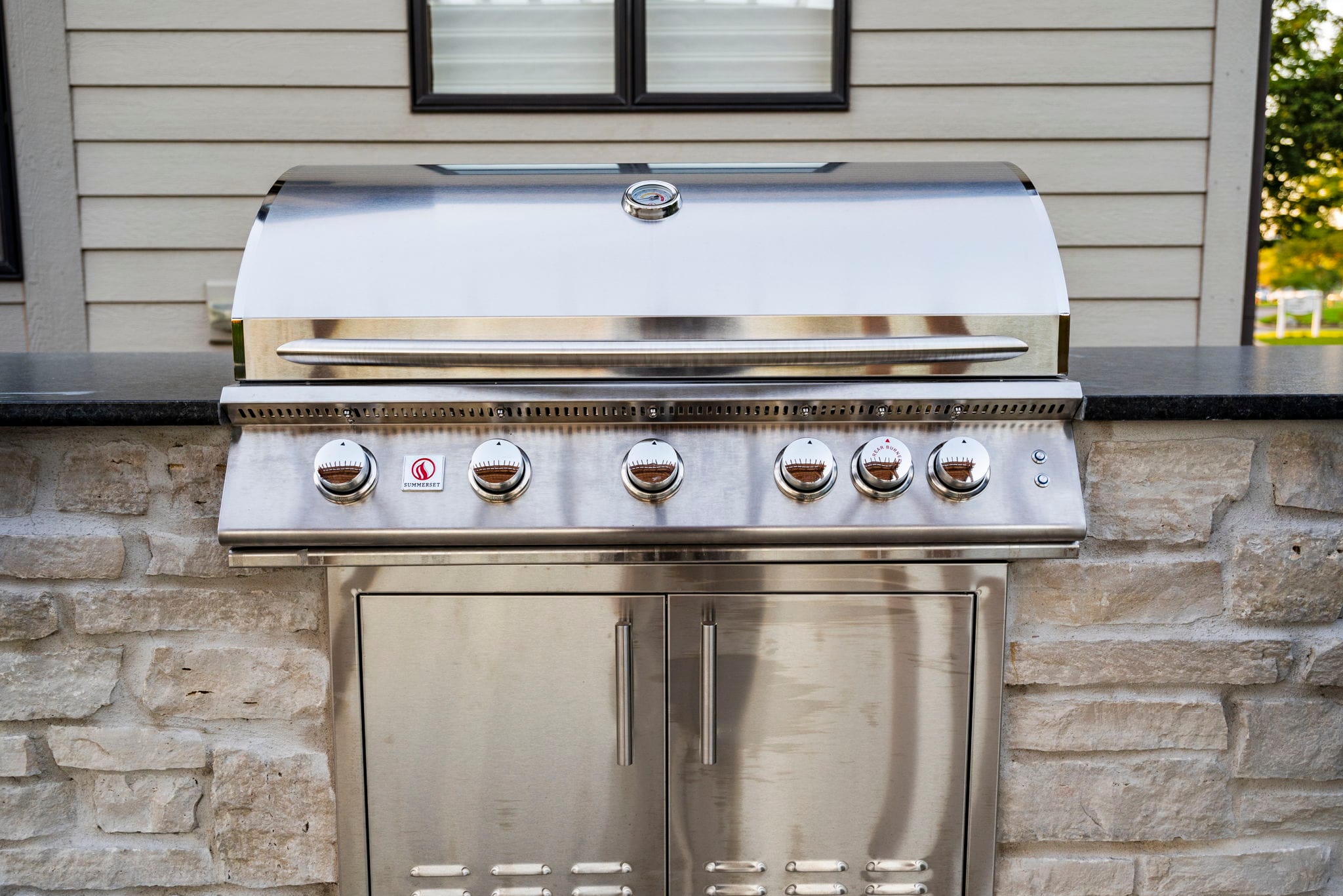Stainless steel built-in grill set into a stone-veneer outdoor kitchen with a black granite countertop