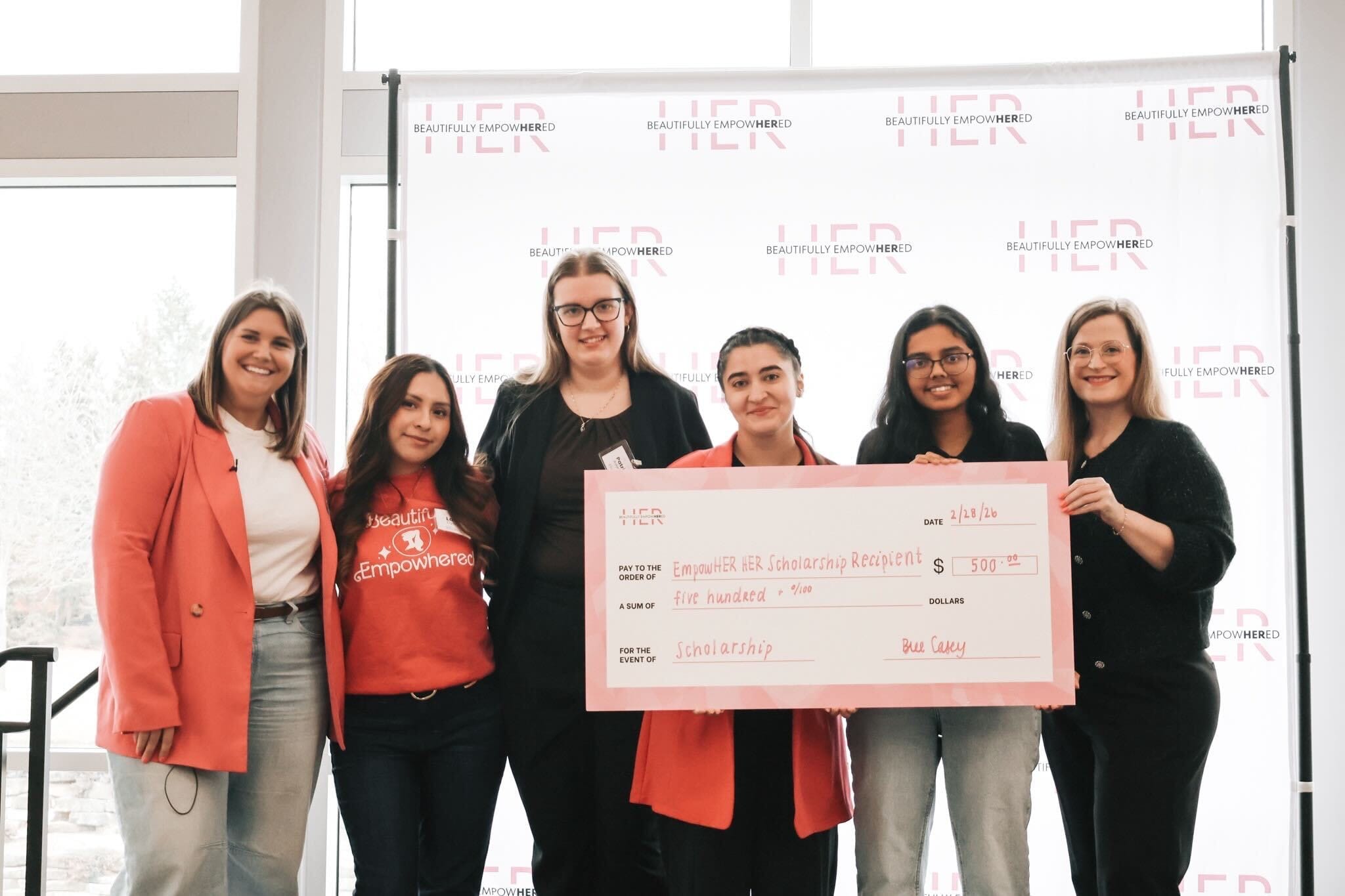 Beautifully EmpowHERed scholarship recipients and organizers presenting a scholarship award during a community event.